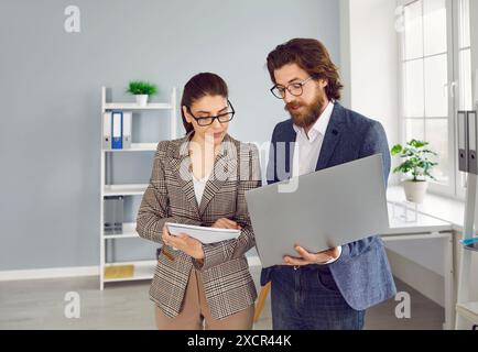 Geschäftsmann, der mit seiner Sekretärin spricht und etwas auf seinem Laptop zeigt Stockfoto
