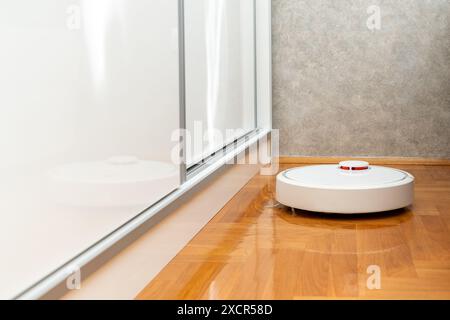 Weißer Roboter-Staubsauger auf dem Holzboden im Schlafzimmer. Reinigung der Wohnung mit einem modernen intelligenten Staubsauger Stockfoto