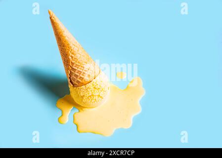 Gelbes Eis schmilzt und verschüttet in Waffelkegel auf pastellblauem Hintergrund. Minimales trendiges, kreatives Sommerrestaurant, Kopierraum. Geschmolzene Schaufel Stockfoto