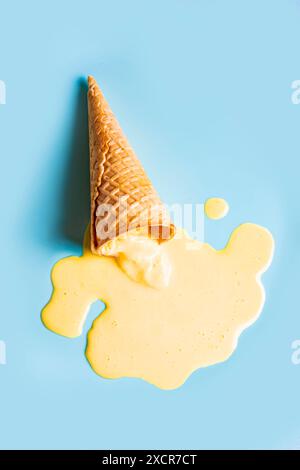 Eiswaffelkegel mit geschmolzenem gelbem Mangoeis auf pastellblauem Hintergrund. Minimalistisches, kreatives Design für Sommergerichte. Stockfoto