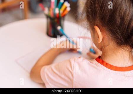 Ein Mädchen zeichnet mit einem Filzstift mit der linken Hand in einem Notizblock auf einem weißen Tisch Stockfoto