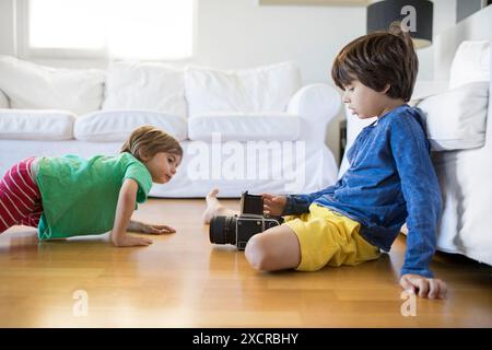 Zwei junge Brüder interagieren spielerisch, wobei ein Bruder eine alte Kamera hält, während der andere aufmerksam zusieht. Sie sind in einer Lichtfüllung Stockfoto