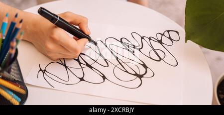 Lady zeichnet mit einem schwarzen Filzstift auf einem weißen Blatt Stockfoto