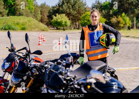Eine Frau mit Sicherheitsweste und Helm steht neben einem Motorrad. Sie lächelt und posiert für ein Foto Stockfoto
