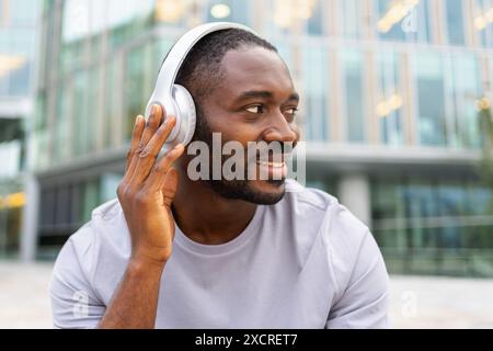 Musiksong-Konzept. Guter Start in den Tag. Glücklicher Afroamerikaner, der moderne Hit auf der Straße in der Stadt hört. Person Guy mit Kopfhörern genießen Sie Ihre Lieblingsmusik im Freien. Lebensfreude der Menschen Stockfoto