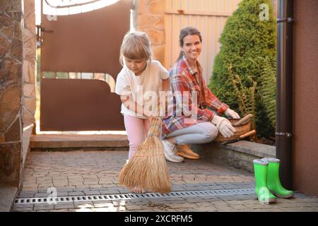 Mutter und ihre süße Tochter putzen zusammen in der Nähe des Hauses am Frühlingstag Stockfoto