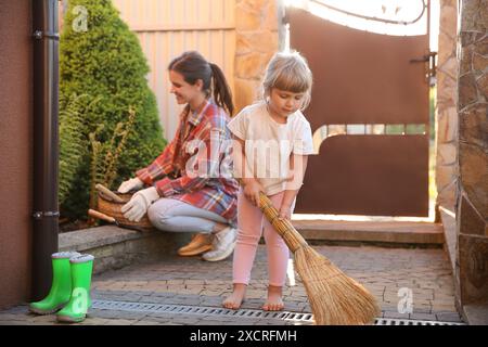 Mutter und ihre süße Tochter putzen zusammen in der Nähe des Hauses am Frühlingstag Stockfoto