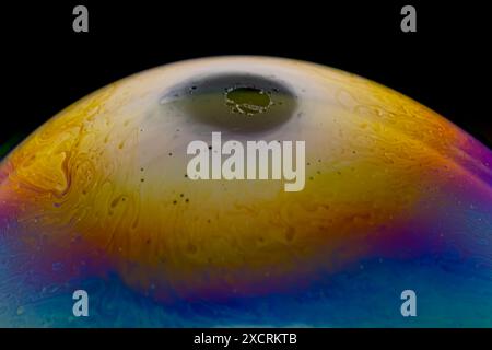 Nahaufnahme, Makroaufnahme einer mehrfarbigen Seifenblase mit gelben, lila, rosa, blauen und grünen Farben auf schwarzem Hintergrund. Stockfoto