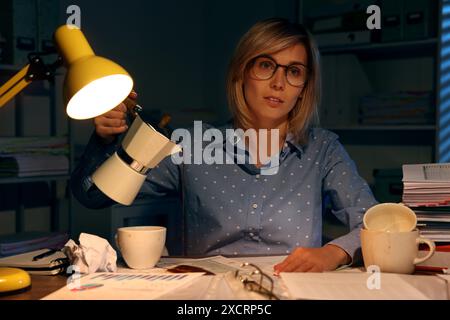 Überforderte Frau, die nachts am Arbeitsplatz im Büro Kaffee an einer Tasse vorbeigießt Stockfoto