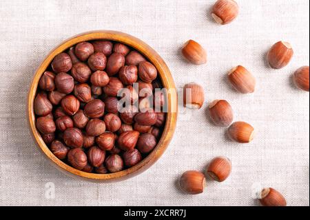 Haselnüsse in einer hölzernen Schüssel auf Leinenstoff. Ganze, getrocknete und geschälte Nüsse von Corylus avellana. Verzehrfertig als Snack und auch zum Backen. Stockfoto