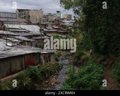 Ein Mann, der auf einem Pfad läuft, der von einem Fluss und Wald begrenzt wird, am Rande des Kibera-Slums in Nairobi Stockfoto