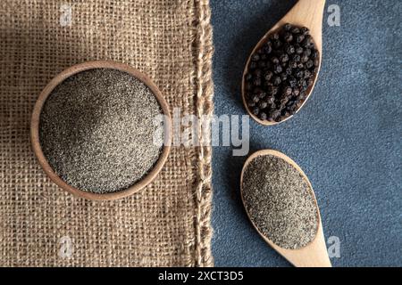 Gemahlener schwarzer Pfeffer mit schwarzen Pfefferkörnern auf dunklem Hintergrund Stockfoto