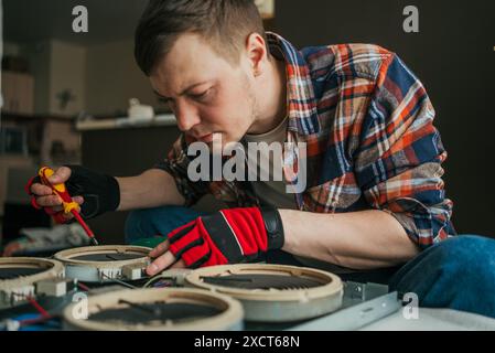 Ein Mann mit kariertem Hemd und Schutzhandschuhen konzentriert sich auf die Reparatur eines elektronischen Geräts. Er arbeitet mit einem Schraubendreher an Bauteilen und zeigt einen akribischen Ansatz. Hausreparatur von Haushaltsgeräten. Stockfoto