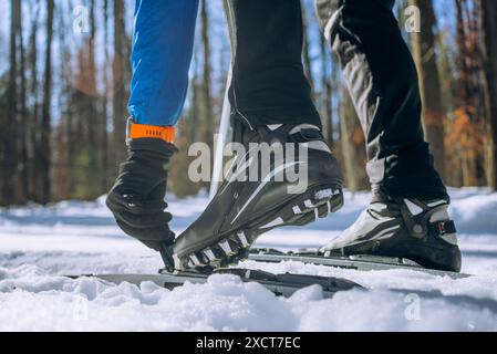 Der Skier schnallt seine Schuhe vor dem Training an Langlaufskiern im Schnee an. Die Beine des Athleten befinden sich in Nahaufnahme, und auf seinem Arm ist eine Fitnessuhr sichtbar, um seinen Puls und sein Lauftempo zu messen. Stockfoto
