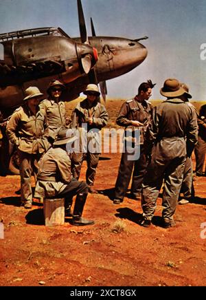 Ein Foto zeigt Luftwaffenoffiziere in Afrika, in tropischer Ausrüstung, die einen Missionsbericht über feindliche Einsätze während des Zweiten Weltkriegs überprüfen. Diese detaillierten Berichte waren von entscheidender Bedeutung für die Bewertung des Erfolgs von Luftmissionen, die Planung künftiger Operationen und die Anpassung von Strategien auf der Grundlage feindlicher Bewegungen und Verteidigungsanlagen. Stockfoto