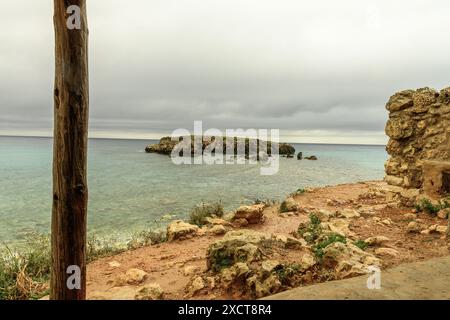 Friedlicher Blick auf den Strand Sant Adeodat auf Menorca, mit einer felsigen Küste, klarem türkisfarbenem Wasser und einem bewölkten Himmel. Ein Holzsteg verläuft entlang Stockfoto