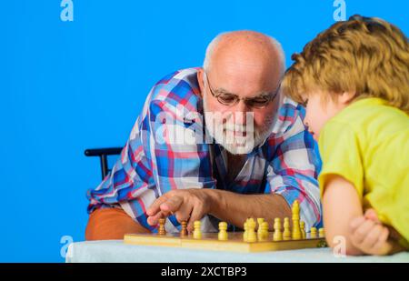 Schachspiel für Kinder. Enkel spielt Schach mit Großvater. Hobby- und Freizeitaktivitäten. Konzentriertes Kind, das Schachstrategie entwickelt. Niedliches kleines Stockfoto