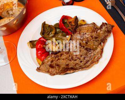 Auf dem runden weißen Teller liegt eine saftige gebratene Scheibe Rinderfilet, garniert mit gedünstetem Gemüse. Stockfoto