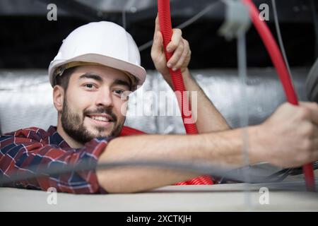 Fachfirma im Dachraum zur Installation eines roten Kabelkanals Stockfoto