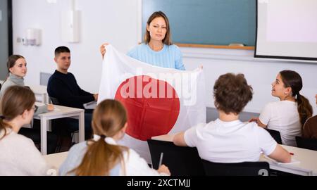 Der Lehrer erzählt den Schülern von Japan und hält eine japanische Flagge in der Hand. Stockfoto