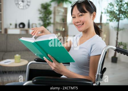 Behinderte asiatische Frau im Rollstuhl liest ein Buch Stockfoto