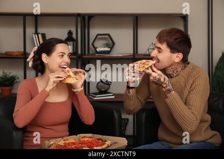 Glückliches junges Paar, das leckere Pizza isst und zu Hause auf Sesseln sitzt Stockfoto