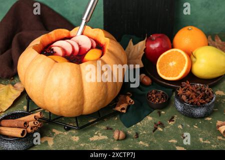 Schöne Komposition mit leckerem Glühwein in Kürbis auf grünem Hintergrund Stockfoto