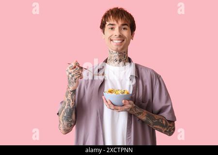Mann hält Schüssel mit Müsliringen und Löffel auf rosa Hintergrund Stockfoto