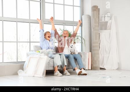 Glückliches reifes Paar mit Farbpaletten und Hund, der während der Reparatur in ihrem neuen Haus auf dem Sofa sitzt Stockfoto
