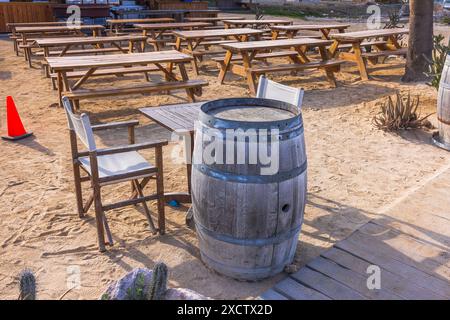 Wunderschöner Blick auf ein leeres Hotelrestaurant im Freien mit Holztischen, Stühlen und einem Tonnentisch auf einer sandigen Oberfläche. Curacao. Stockfoto