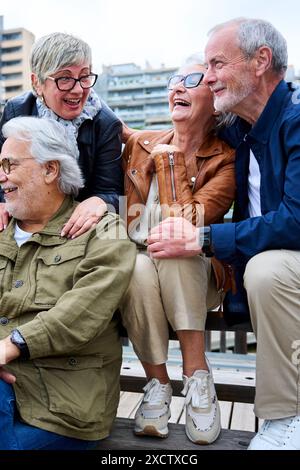 Eine Gruppe älterer kaukasischer Freunde, die Spaß haben, zusammen zu lachen und auf der Bank in der Stadt sitzen. Stockfoto
