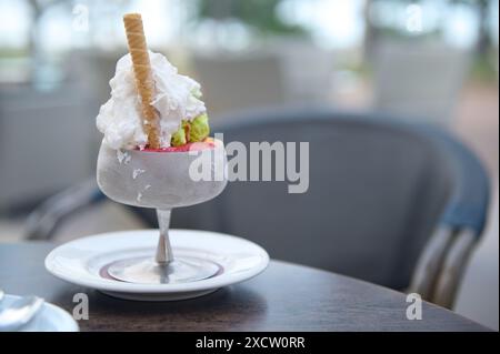 Nahaufnahme eines köstlichen Eisbecher mit Schlagsahne und Waffelstab, serviert in einem Milchglas auf einem Café-Tisch im Freien. Stockfoto