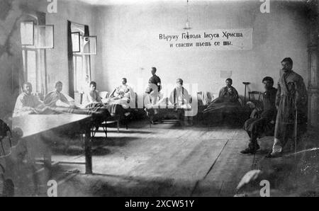 Ein Schwarzweiß-Foto aus dem Jahr 1876, das das Innere eines Krankenhauses des Roten Kreuzes für russische Soldaten darstellt. Das Bild zeigt acht Männer, einige in Betten und andere mit Krücken, die von einem Pfleger und einer Krankenschwester betreut werden. Auf einem Banner an der Rückwand steht: Glauben Sie an unseren Herrn Jesus Christus, und Sie werden gerettet werden in russisch-bulgarisch galizisch, und eine Botschaft des Glaubens und der Heilung. Stockfoto