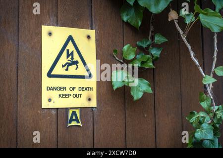 Gelbes Warnschild „Gefahr des Todes halten Sie draußen“ und „Hochspannung“ auf einem Holzzaun Stockfoto