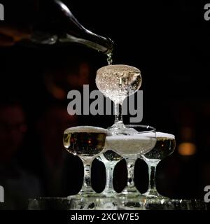 Kellner gießt Champagner auf einem Pyramidenturm auf dunklem Hintergrund Stockfoto