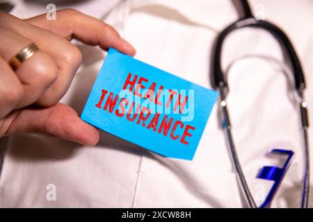 Krankenversicherung, Krankenversicherungskonzept. Krankenversicherungstext auf einer weißen Visitenkarte auf blauem Hintergrund mit Stethoskop, Pillen in einer Komposition Stockfoto