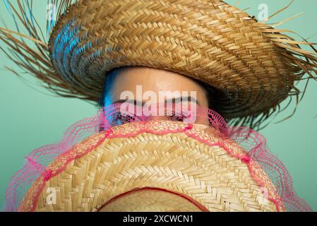 Nahporträt einer schönen Frau, die einen Strohhut mit einem anderen Hut vor ihrem Gesicht trägt. Saint Johns Festival. Isoliert auf hellgrünem Hintergrund Stockfoto