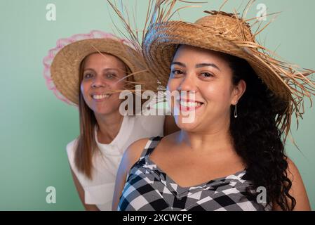 Zwei schöne Frauen mit traditionellen Strohhüten vom Sao Joao Festival, die in die Kamera schauen. Isoliert auf hellgrünem Hintergrund. Stockfoto