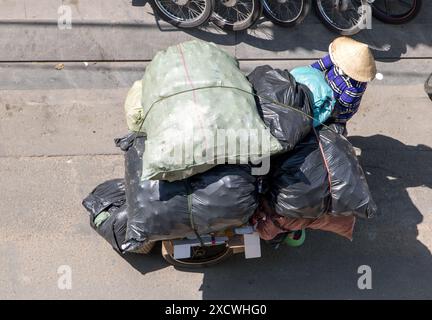 Sammlung von recycelbaren Abfällen in den Straßen von Ho Chi Minh. Vietnamesische Leute schieben einen Wagen voller Taschen, Saigon City. Stockfoto