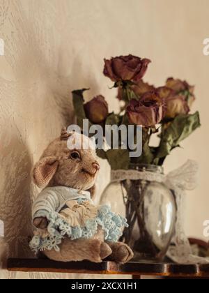 Vintage Eleganz: Teddy Lamb and Roses: Ein vertikales Stillleben mit einem bezaubernden Teddylamm in einem blauen Spitzenkleid, begleitet von einem Stockfoto