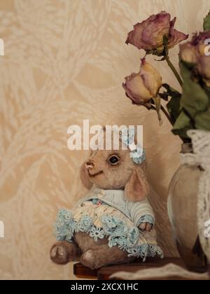 Vintage Eleganz: Teddy Lamb and Roses: Ein vertikales Stillleben mit einem bezaubernden Teddylamm in einem blauen Spitzenkleid, begleitet von einem Stockfoto