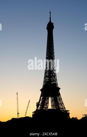 Paris, Frankreich - 07. Juni 2024: Silhouette des Eiffelturms im frühen Morgenlicht. Logo der Olympischen Spiele auf dem Turm und Baukran auf dem Boden. Stockfoto