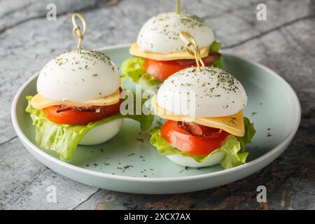 Originelles Frühstück auf Spießen mit hart gekochten Eiern mit Käse, Speck, Tomaten und Salat in Nahaufnahme auf einem Teller auf dem Tisch. Horizontal Stockfoto