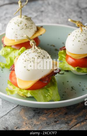 Festliches Ei-Sandwich mit Käse, Speck, Tomaten und Salat in Nahaufnahme auf einem Teller auf dem Tisch. Vertikal Stockfoto