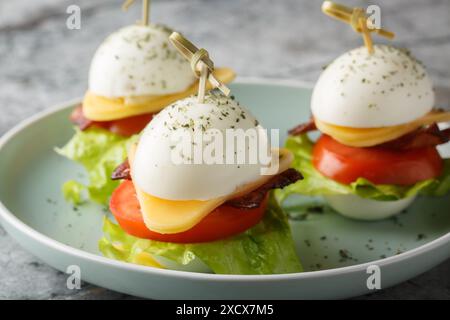 Snack-Sandwiches aus Eiern mit Käse, Speck, Tomaten und Salat in Nahaufnahme auf einem Teller auf dem Tisch. Horizontal Stockfoto