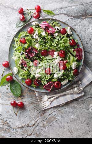 Eingelegte Kirsche, Ziegenkäse und Rucolasalat mit Balsamico-Sauce in Nahaufnahme auf einem Teller auf dem Tisch. Vertikale Draufsicht von oben Stockfoto