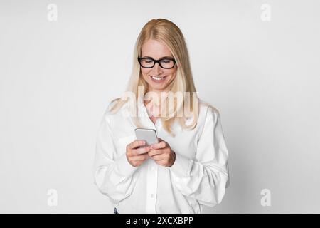 Lächelnde Frau in weißem Shirt verwendet Smartphone vor weißem Hintergrund Stockfoto