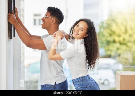 Ein Paar, glücklicher und hängender Bilderrahmen in einem neuen Haus für Renovierungen, Kreativität und Verbundenheit für die Innenarchitektur zusammen. Menschen, Beziehung und Stockfoto