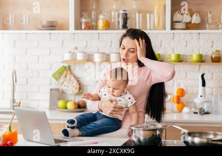 Mutter Balancing Arbeit und Kinderbetreuung in einer modernen Küche Stockfoto