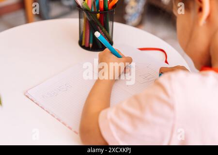 Ein Mädchen zeichnet mit einem Filzstift mit der linken Hand in einem Notizblock auf einem weißen Tisch Stockfoto